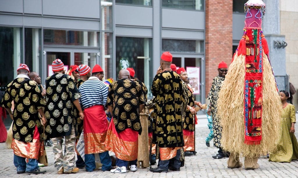 Colourfully dressed villagers presenting large yam tubers at a harvest festival celebration