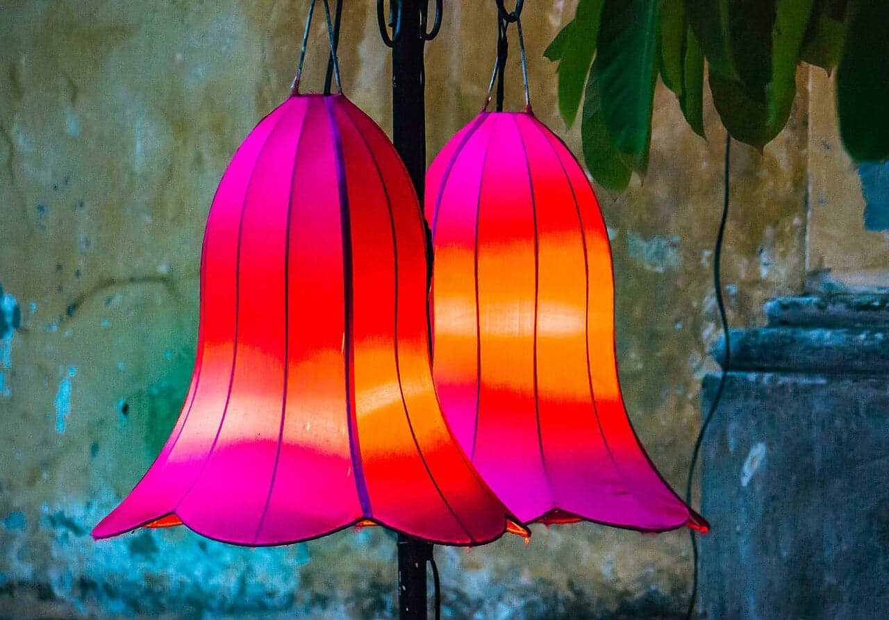 Two brightly coloured pink and orange silk lanterns shaped like flowers, hanging on a wall in Hoi An