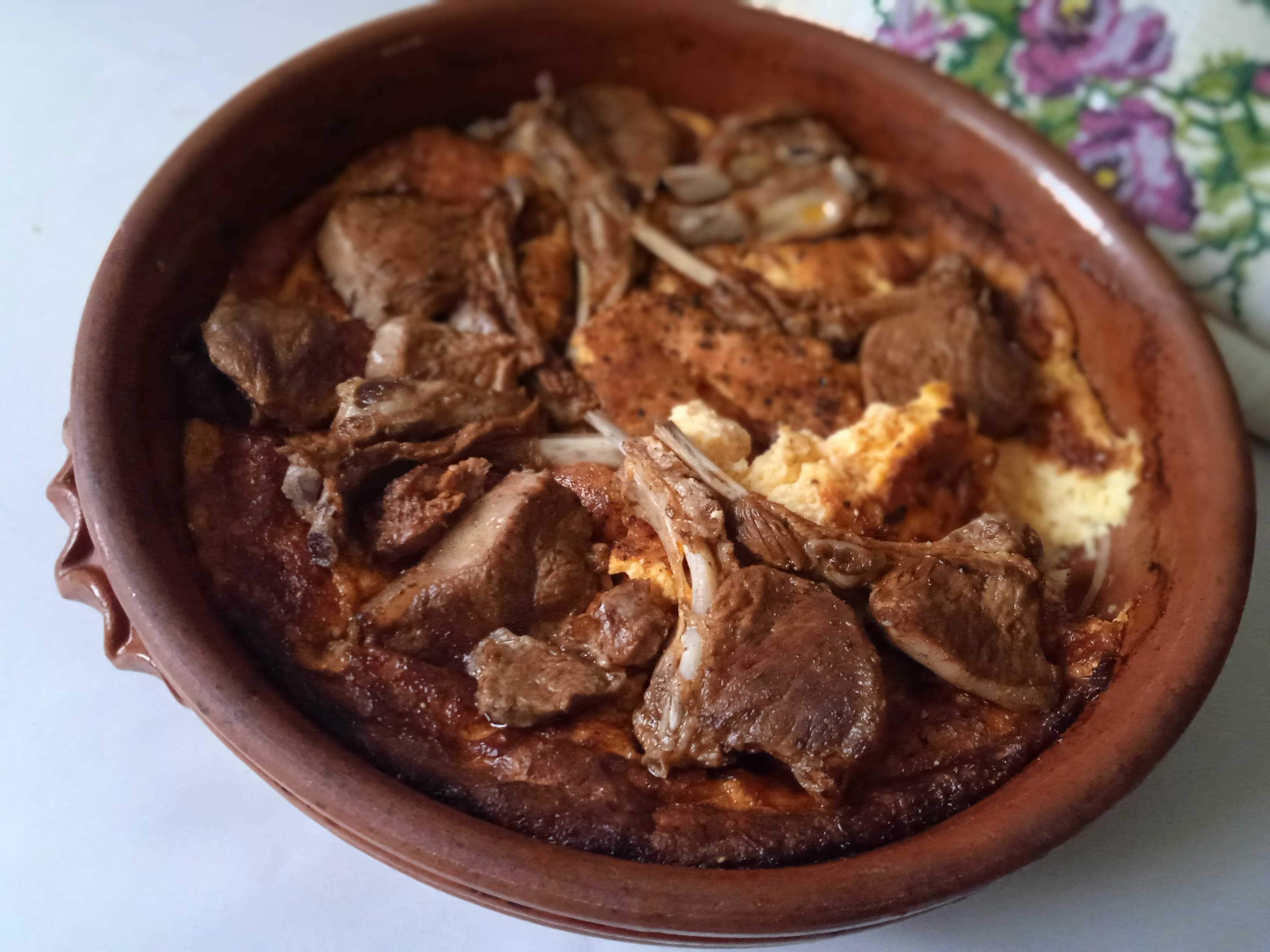 A clay dish of tavë kosi with a golden baked yogurt topping