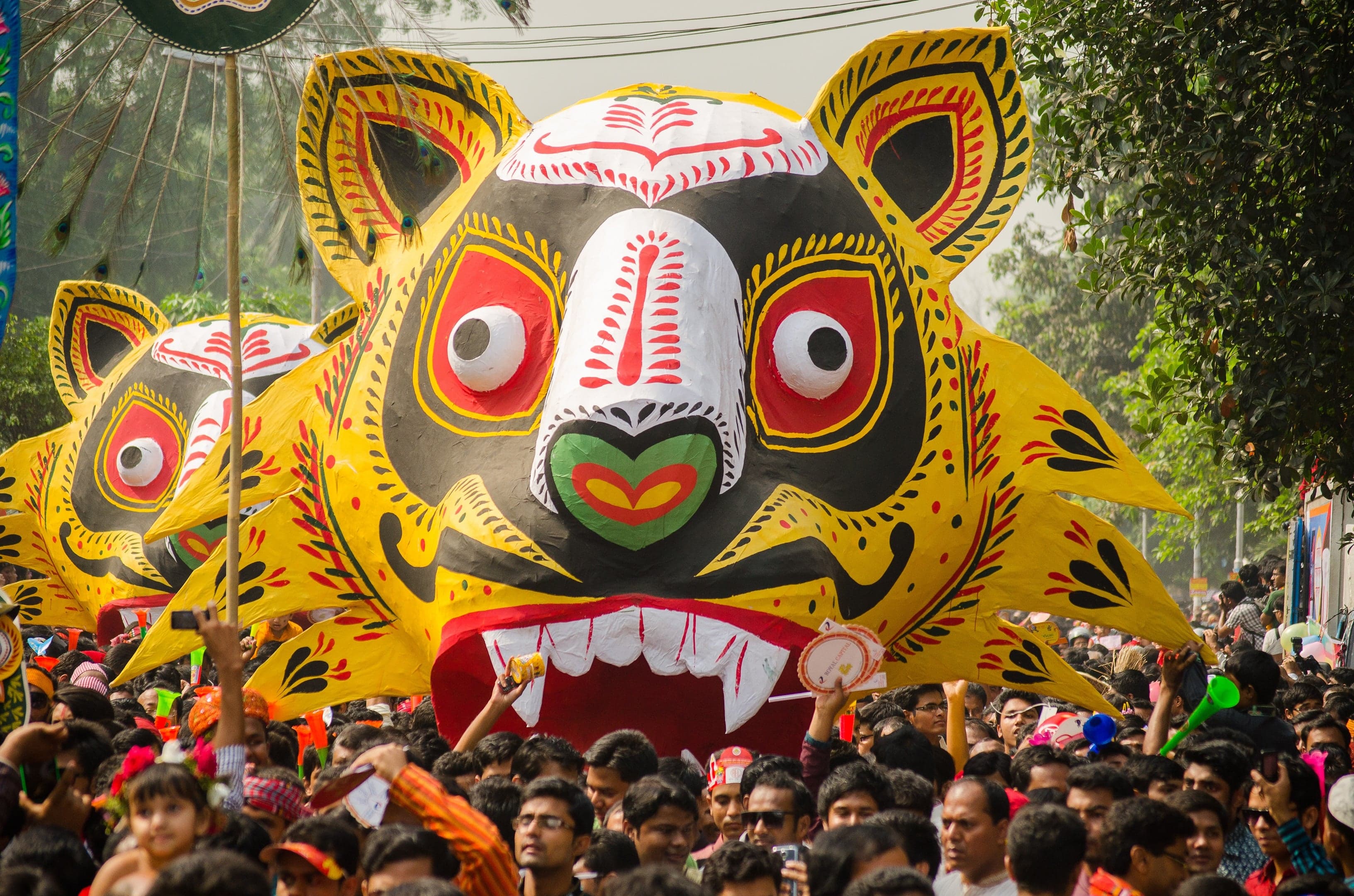 A giant colourful tiger mask being carried through a crowded street in Dhaka during the Pohela Boishakh procession