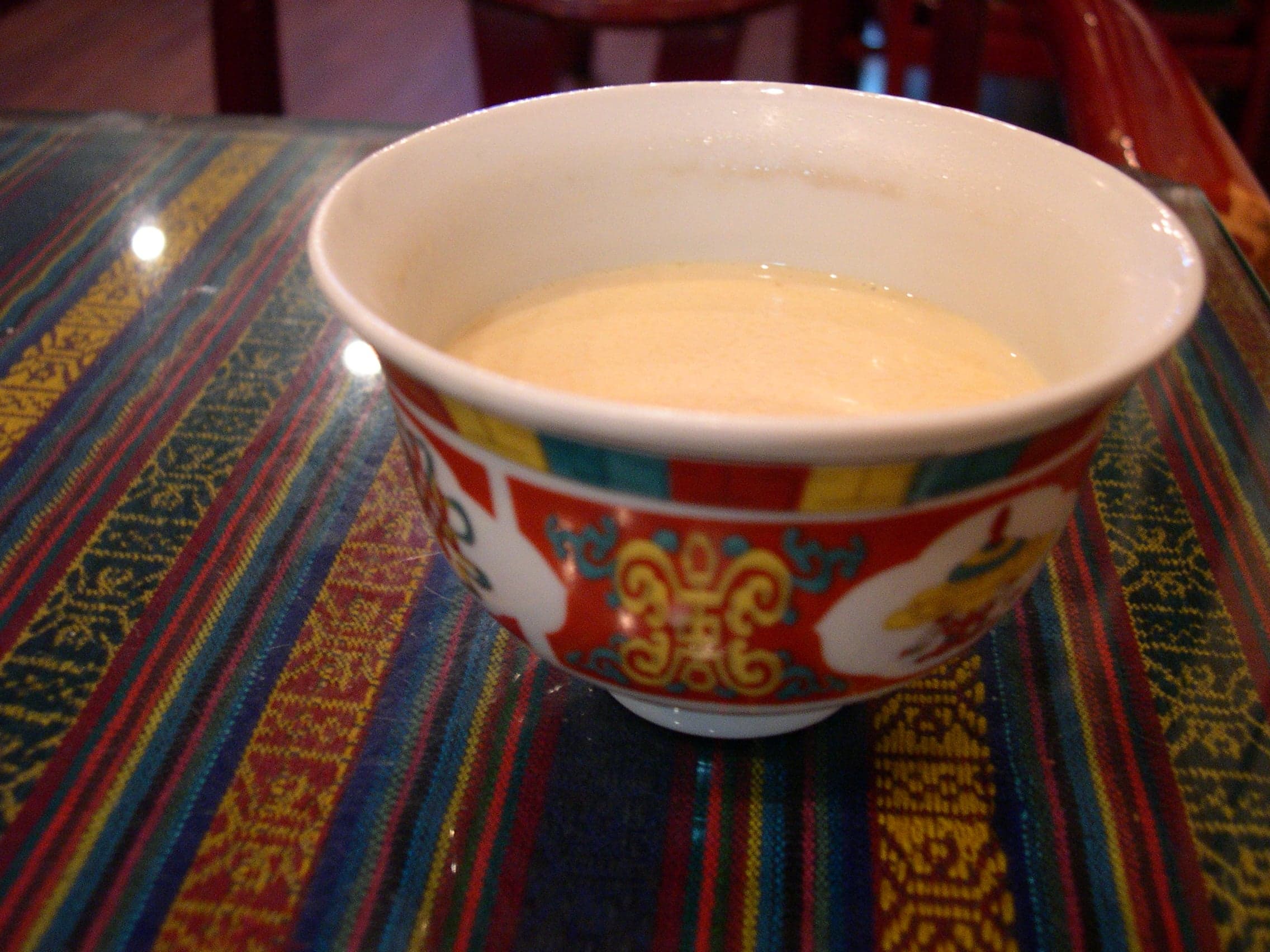 A wooden bowl of pale yellow Bhutanese butter tea with steam rising from it