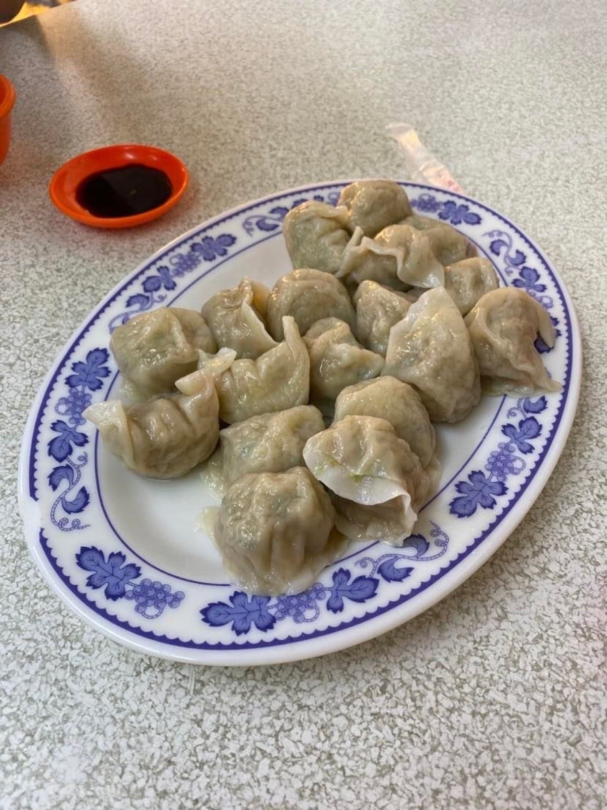 A plate of steamed Chinese dumplings with a small dish of sauce