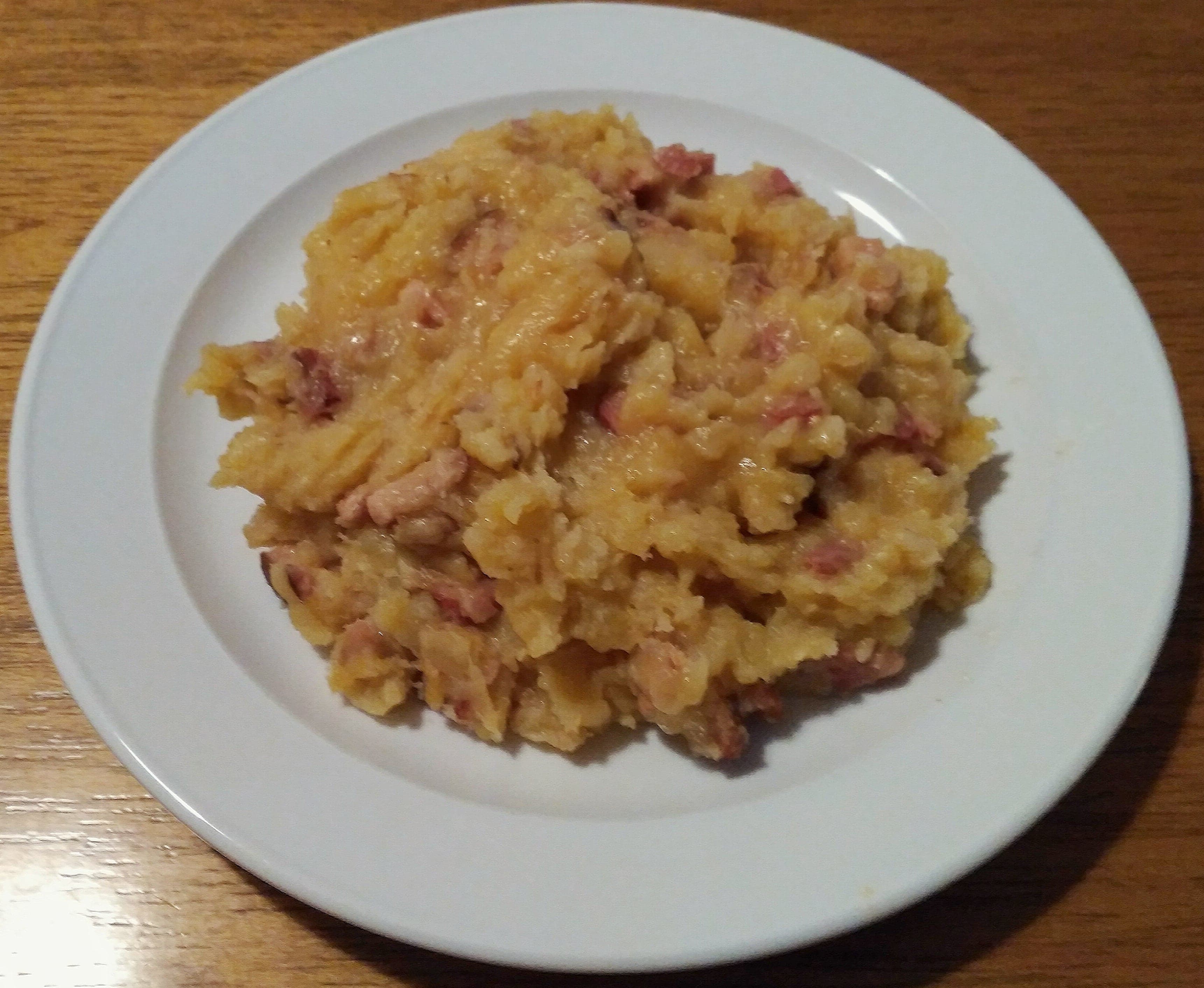 A bowl of thick creamy mulgipuder porridge topped with crackling on a wooden table
