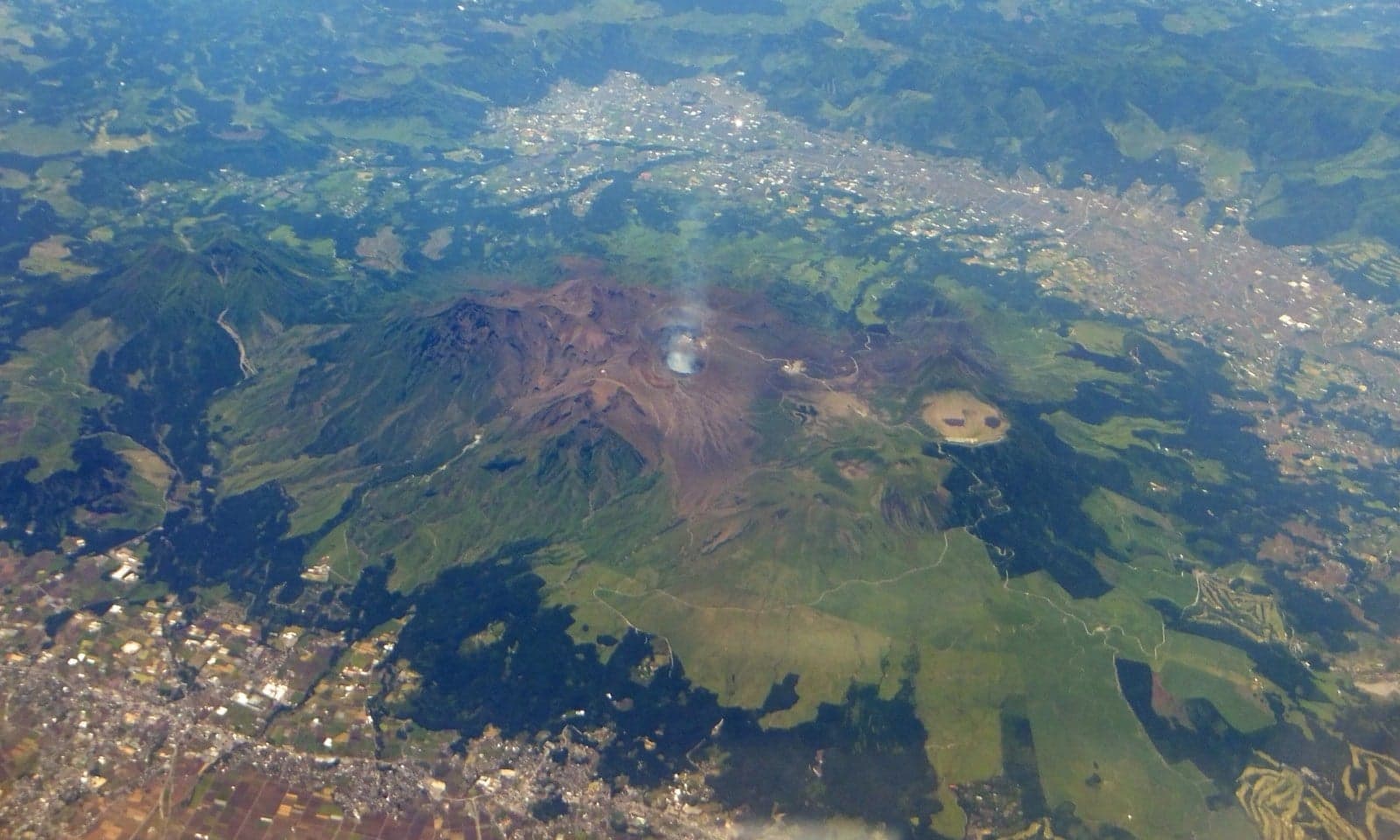 An aerial view of Mount Aso, an enormous Japanese volcano with steam rising from its crater
