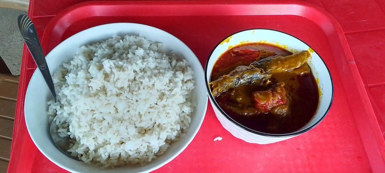A bowl of Liberian palm butter soup served over white rice, with pieces of meat and green leaves
