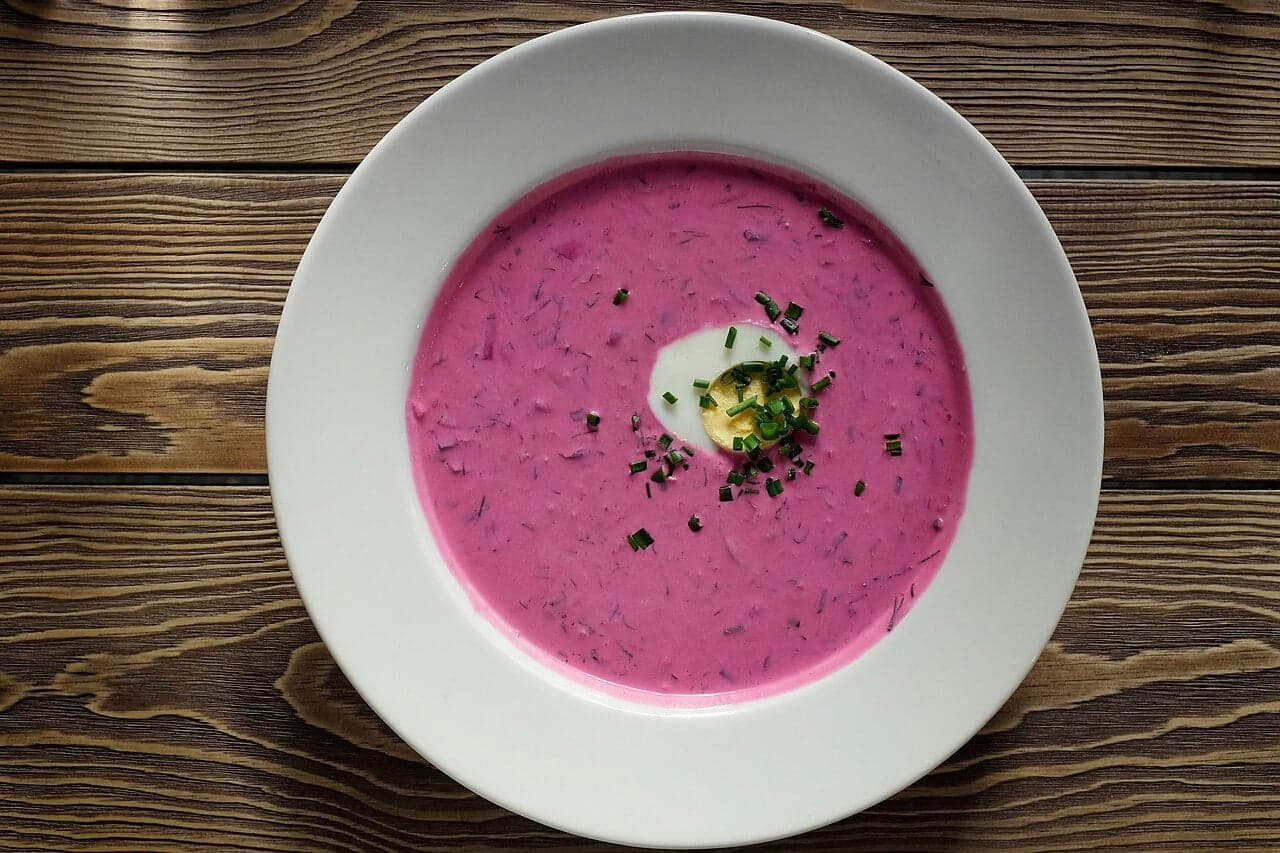 A bowl of vivid pink cold beet soup topped with cucumber and dill, served with a boiled egg