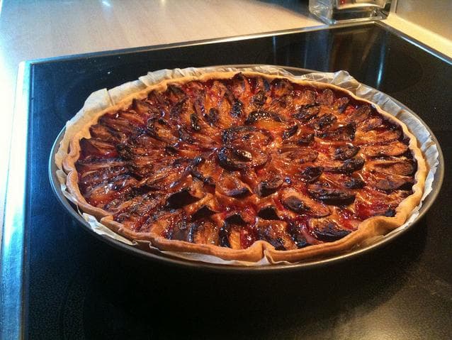 A quetsch tart with rows of blue plum halves on golden pastry