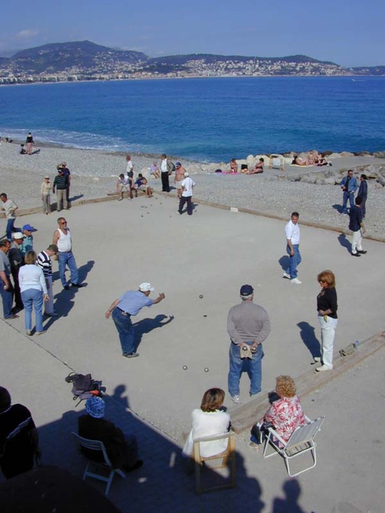 People playing petanque, rolling silver metal balls on a sandy pitch