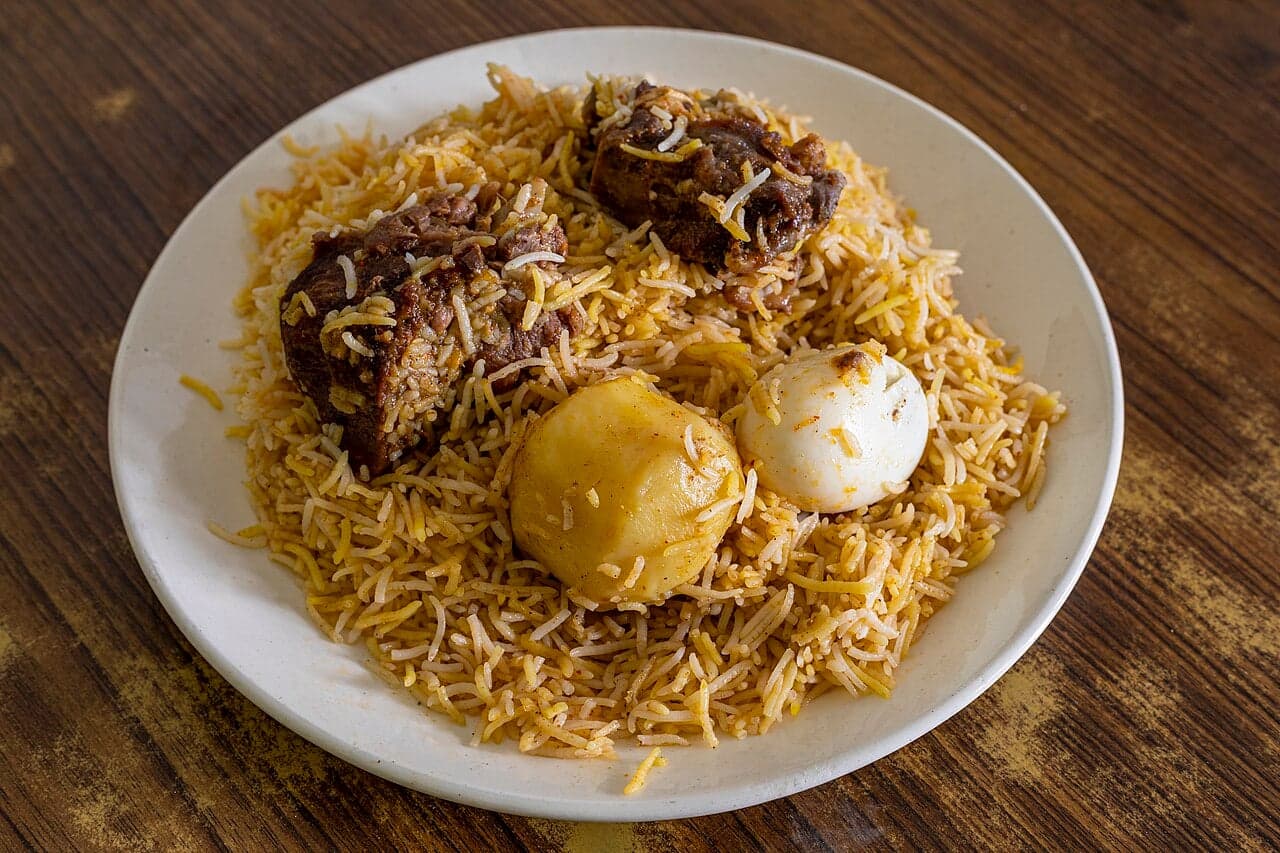 A large pot of Mauritian biryani with rice, spices and meat, garnished with fried onions