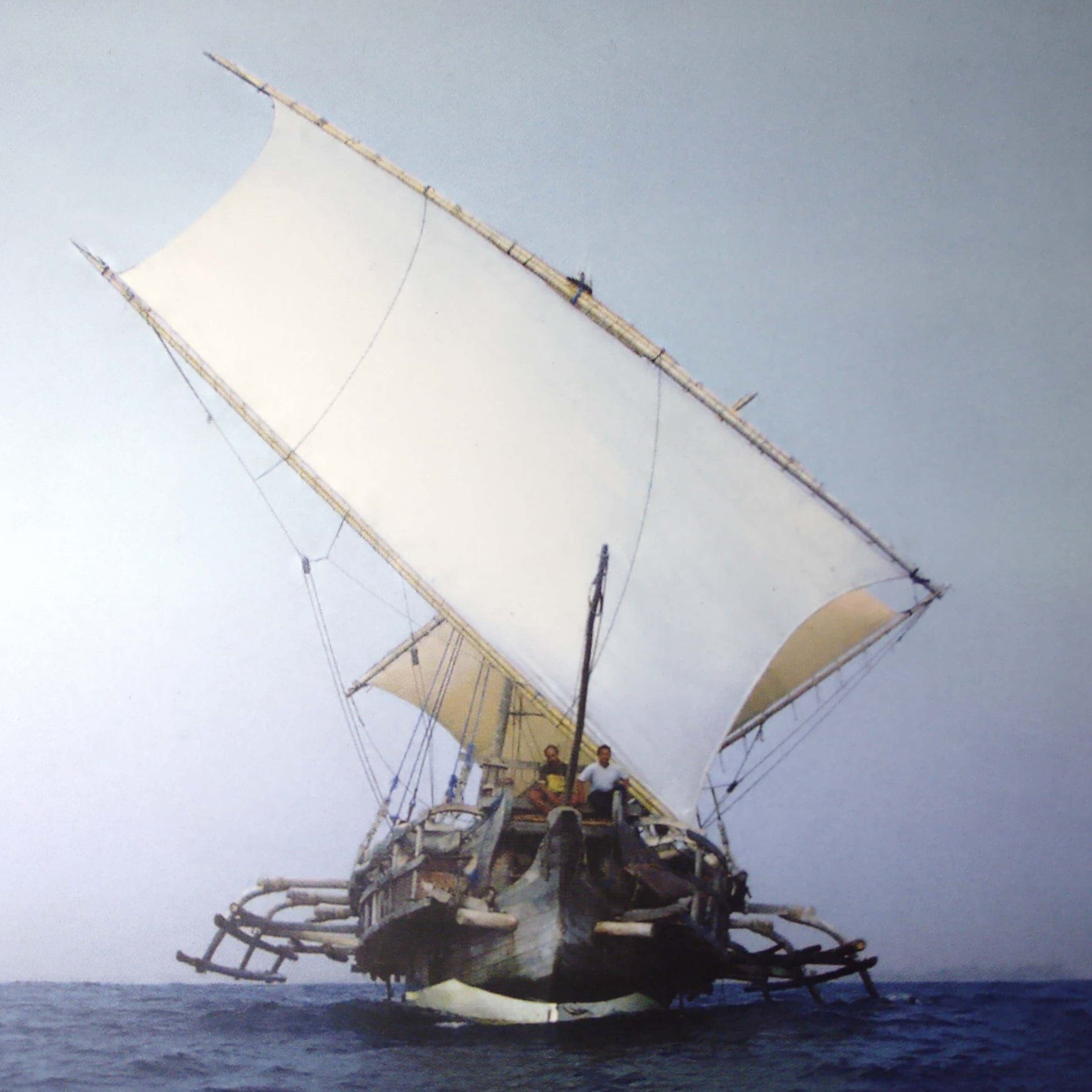 A traditional Micronesian outrigger canoe with a sail on calm Pacific water