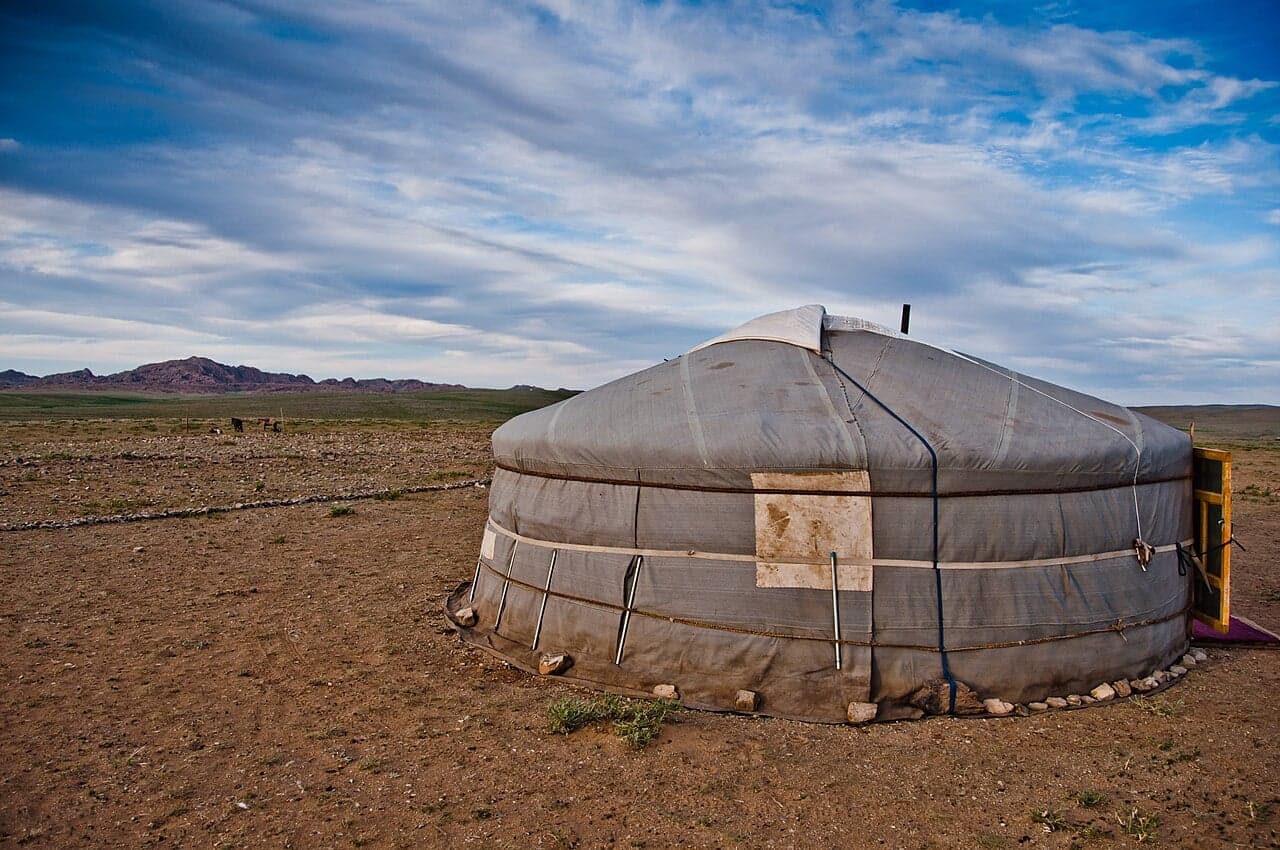 A white felt ger sitting on the Mongolian steppe with mountains behind
