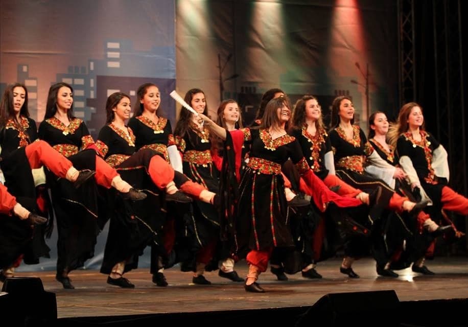 A line of dancers in traditional dress performing dabke with linked arms