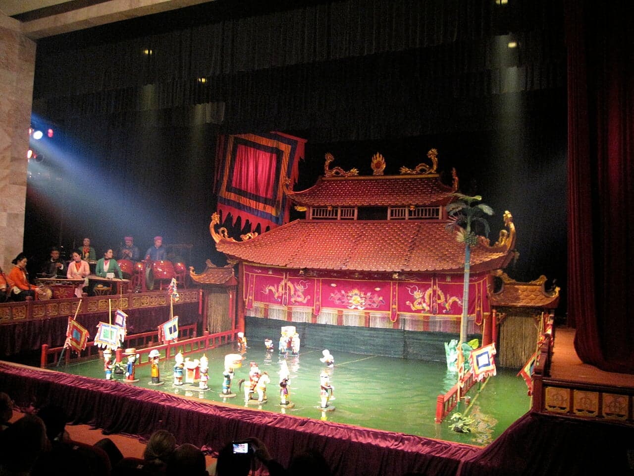 A water puppet performance at the Thang Long theatre in Hanoi, with colourful wooden puppets dancing on a pool of water in front of an ornate red and gold backdrop